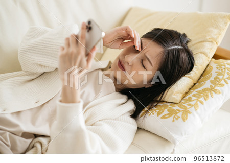 Woman watching smartphone on sofa 96513872