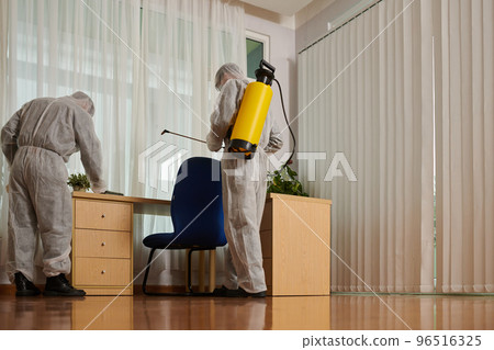 Disinfection service company staff in protective workwear carrying out their work in house Disinfection service company staff in protective workwear carrying out their work in house 96516325
