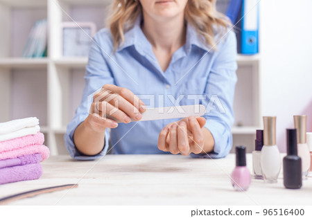 woman aligns her nails with a nail file. Alignment of the nail edge. Manicure at home for yourself. A woman's hand with healthy natural nails. procedure of nail care 96516400
