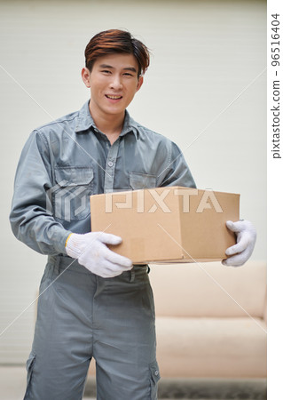 Portrait of positive Vietnamese mover holding cardboard box, house moving and delivery concept Portrait of positive Vietnamese mover holding cardboard box, house moving and delivery concept 96516404
