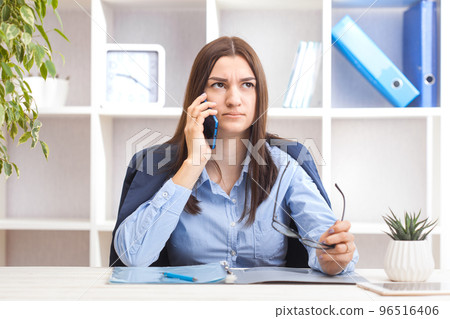 Young beautiful woman sitting in a chair and talking on the phone at her working place. 96516406