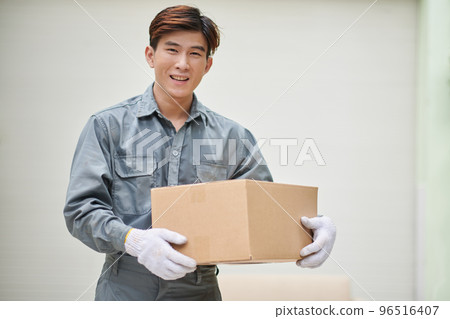Smiling mover in grey uniform holding cardboard box Smiling mover in grey uniform holding cardboard box 96516407