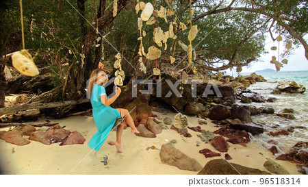 Pretty woman swinging on a swing on a tropical beach, on shores of the turquoise sea. Concept travel, walks, rest in sea, tropical resort coastline relaxation traveling tourism summer holidays. Pretty woman swinging on a swing on a tropical beach, on shores of the turquoise sea. Concept travel, walks, rest in sea, tropical resort coastline relaxation traveling tourism summer holidays. 96518314