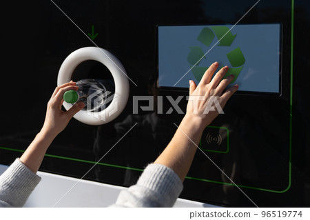 Woman uses a self service machine to receive used plastic bottles 96519774