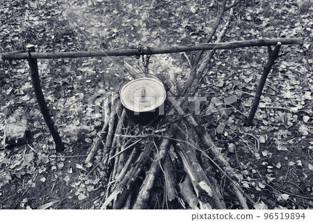 Black and white retro. Cooking in old sooty cauldron on campfire at glade Black and white retro. Cooking in old sooty cauldron on campfire at glade 96519894