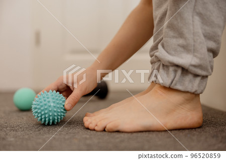 Woman doing flatfoot correction gymnastic exercise using massage ball. Myofascial relaxation of foot muscles. Hallux valgus. Pain. Identification of flat feet. Self care practices at home, healthcare. 96520859