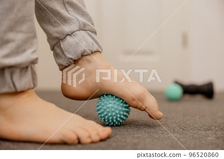 Woman doing flatfoot correction gymnastic exercise using massage ball. Myofascial relaxation of foot muscles. Hallux valgus. Pain. Identification of flat feet. Self care practices at home, healthcare. Woman doing flatfoot correction gymnastic exercise using massage ball. Myofascial relaxation of foot muscles. Hallux valgus. Pain. Identification of flat feet. Self care practices at home, healthcare. 96520860