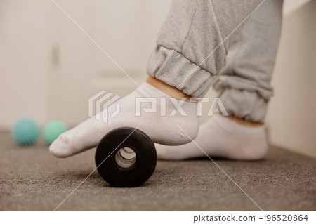 Woman doing flatfoot correction gymnastic exercise using massage roller. Myofascial relaxation of foot muscles. Hallux valgus. Pain. Identification of flat feet. Self care practices at home, health. 96520864