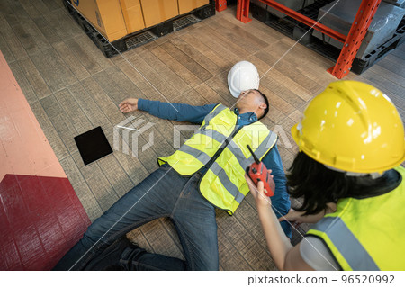 A female warehouse worker using a walkie-talkie called the factory's first aid team to rescue an unconscious man. pass out or blackout, unsafe, emergency 96520992