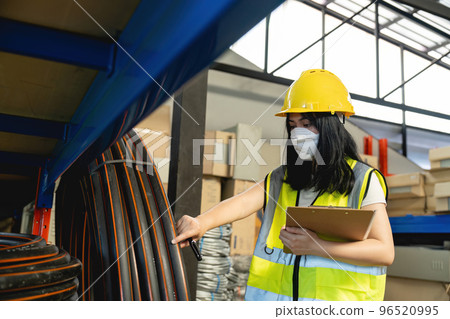 Asian woman wearing reflective jacket holding checklist paper standing in factory warehouse. 96520995