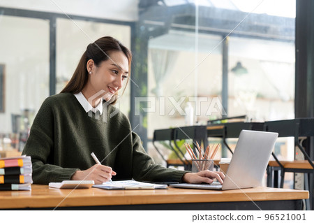 Portrait young asian studying remotely from home, using a laptop, taking notes on notepad during online lesson, e-learning concept, smiling 96521001