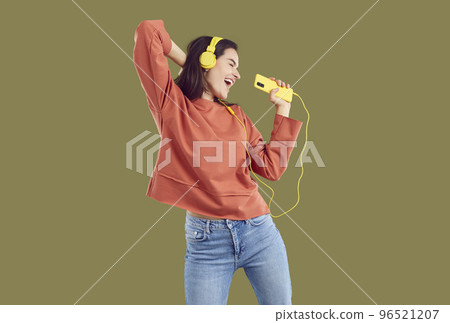 Brunette woman in red sweatshirt and jeand listening music using yellow smartphone and headset. Brunette woman in red sweatshirt and jeand listening music using yellow smartphone and headset. 96521207