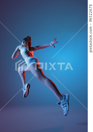 Back view of young sportive girl in white sportswear running away isolated over gradient blue purple background in neon light. Fitness, hobby, healthy lifestyle 96522678