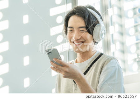A young man wearing headphones and listening to music on his smartphone in the sunlight filtering through the trees 96523557