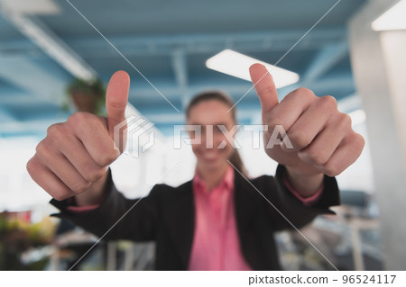 Beautiful cheerful businesswoman showing double thumbup advert at workplace in creative open space coworking office 96524117