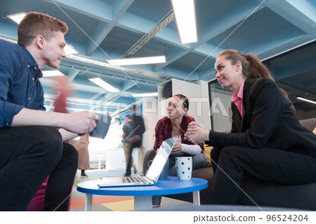 Multiethnic startup business team on meeting in a modern bright open space coworking office. Brainstorming, working on laptop. Group of coworkers walking around in motion blur. 96524204