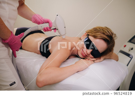 A girl in black underwear does laser hair removal on her back in the salon 96524819