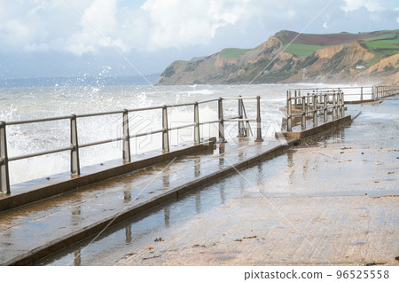 Big waves and water splashes at West Bay beach near Bridgport in Dorset, United Kingdom. Walkway or promenade along the beach, selective focus 96525558
