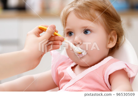 feeds baby with a spoon porridge. A little girl feeds baby with a spoon porridge. A little girl 96530509