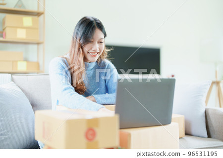 Starting small business entrepreneur of independent Asian woman smiling using computer laptop with cheerful success of online marketing package box items and SME delivery concept. 96531195