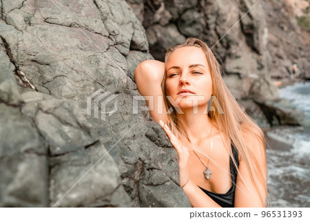 Woman swimsuit sea. Attractive blonde woman in a black swimsuit enjoying the sea air on the seashore around the rocks. Travel and vacation concept. 96531393