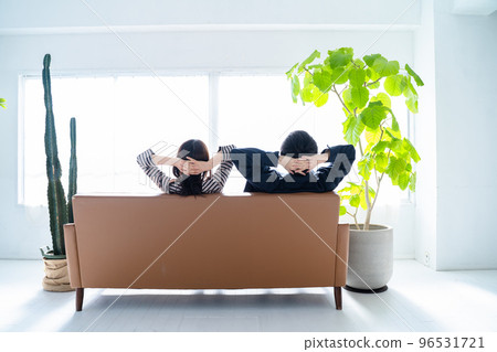 A couple sitting on the sofa and cuddling from behind-living room with bright foliage plants 96531721