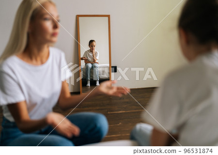 Reflection in mirror detached sad little girl during stressed mother scolding, shouting and gesturing with hands at stubborn difficult child daughter at home. Concept of family problems, conflict. 96531874