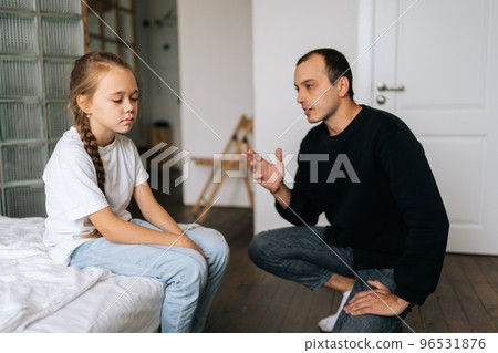 Portrait of young father having serious conversation with naughty spoiled female child, talking about rules to her sitting on bed at home. Concept of dad-daughter problem in preteen years. Portrait of young father having serious conversation with naughty spoiled female child, talking about rules to her sitting on bed at home. Concept of dad-daughter problem in preteen years. 96531876