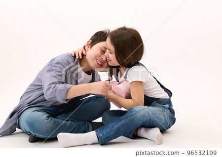 Happy Caucasian little girl in blue denim overalls, rejoices in receiving a cute heart shaped pink gift box from her brother, gently hugging him. Saint Valentines Day. February 14. Women's Day. March 96532109