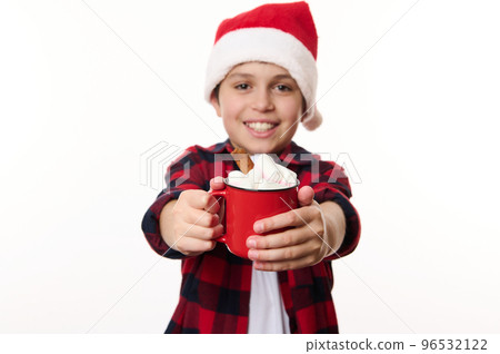 Details: a cup of hot chocolate with marshmallows, in the hands of a blurred cheerful Caucasian school boy in Santa hat, smiling to the camera, isolated on white background with copy advertising space Details: a cup of hot chocolate with marshmallows, in the hands of a blurred cheerful Caucasian school boy in Santa hat, smiling to the camera, isolated on white background with copy advertising space 96532122