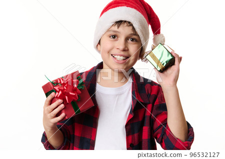 Adorable Hispanic boy wearing Santa hat, smiling a beautiful toothy smile, posing with Christmas gifts, looking at camera. New Years preparations. Winter holidays, magical festive atmospheric mood Adorable Hispanic boy wearing Santa hat, smiling a beautiful toothy smile, posing with Christmas gifts, looking at camera. New Years preparations. Winter holidays, magical festive atmospheric mood 96532127