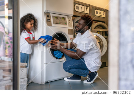 Man and his daughter putting laundry into a washer 96532302