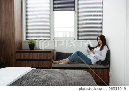 Woman reading book in a bedroom with bed and wooden wardrobe in modern apartment Woman reading book in a bedroom with bed and wooden wardrobe in modern apartment 96533049