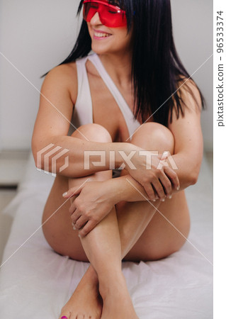 a slender woman is sitting on a bed in a beauty salon before laser hair removal. look at the delicate skin on your legs and want to make it more hairless 96533374
