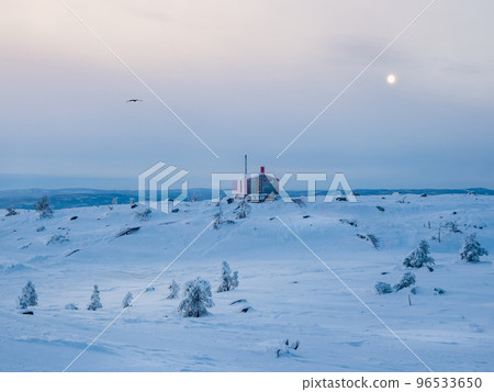 Lonely red bungalowon a snowy frosty hill under dark evening sky with a full moon. Minimalistic background with of lonely red cabin in winter. 96533650