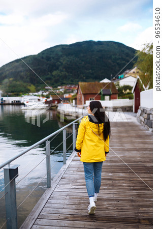 Young woman enjoys picturesque landscape. The girl tourist in a yellow jacket posing in the Norway. Young woman enjoys picturesque landscape. The girl tourist in a yellow jacket posing in the Norway. 96534610