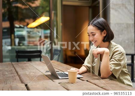 Portrait of asian woman looking at laptop, video chat, talking with someone via computer camera, sitting in cafe and drinking coffee, online meeting Portrait of asian woman looking at laptop, video chat, talking with someone via computer camera, sitting in cafe and drinking coffee, online meeting 96535113