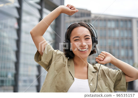 Girl dances on street with headphones on, listens to music and feels happy walking in city Girl dances on street with headphones on, listens to music and feels happy walking in city 96535157