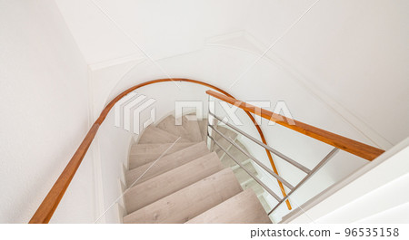 Spiral stairway with white stairs and wooden railing on wall inside of a house. Spiral stairway with white stairs and wooden railing on wall inside of a house. 96535158