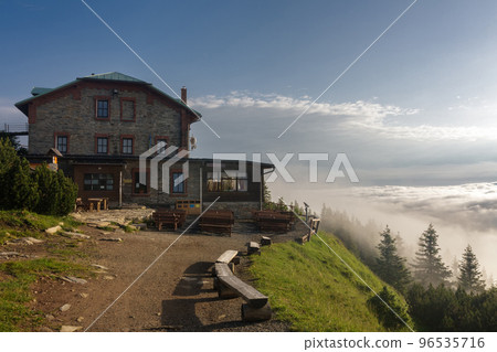 Old stone mountain cottage in Jeseniky mountains on a summer foggy morning and sea of clouds around mountain peak Old stone mountain cottage in Jeseniky mountains on a summer foggy morning and sea of clouds around mountain peak 96535716