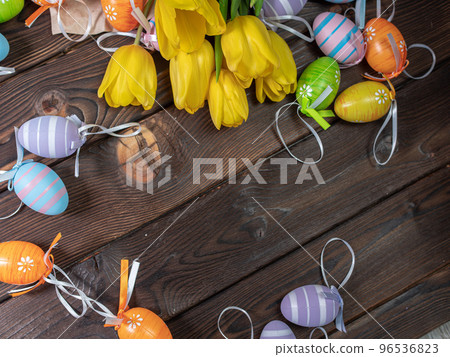 Several spring yellow tulips lie on a wooden board next to Easter eggs 96536823
