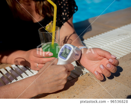 Two girlfriends girls in medical masks in the pool measure the temperature with a non-contact thermometer Two girlfriends girls in medical masks in the pool measure the temperature with a non-contact thermometer 96536828