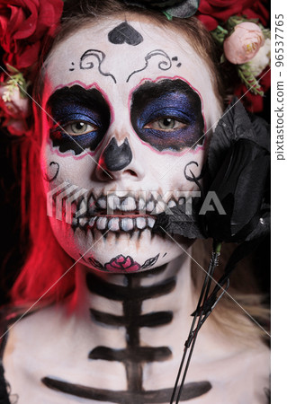 Woman wearing santa muerte body art in studio, acting glamorous on day of the dead mexican celebration. Ritual skull body art with black and white, posing with roses and flower crown. Woman wearing santa muerte body art in studio, acting glamorous on day of the dead mexican celebration. Ritual skull body art with black and white, posing with roses and flower crown. 96537765