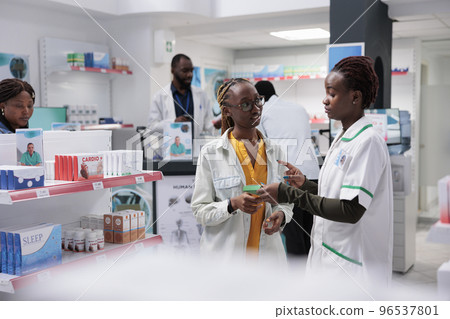 African american pharmacist helping woman buying food supplements in drugstore. Medicaments retail, client and pharmacy store consultant talking, buyer choosing medications African american pharmacist helping woman buying food supplements in drugstore. Medicaments retail, client and pharmacy store consultant talking, buyer choosing medications 96537801