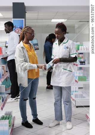 African american pharmacist helping woman choosing medications in drugstore. Client and pharmacy consultant chatting, customer buying medicaments, wide shot, all black team African american pharmacist helping woman choosing medications in drugstore. Client and pharmacy consultant chatting, customer buying medicaments, wide shot, all black team 96537807