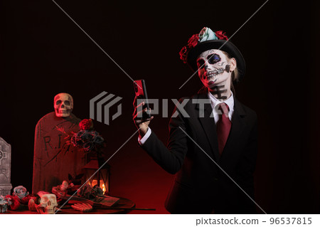 Beautiful woman with santa muerte make up taking photos with smartphone, celebrating day of the dead holiday mexican tradition. Taking pictures with halloween body art, traditional celebration. Beautiful woman with santa muerte make up taking photos with smartphone, celebrating day of the dead holiday mexican tradition. Taking pictures with halloween body art, traditional celebration. 96537815