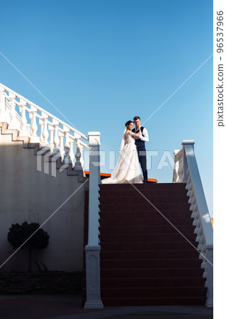 The bride and groom on the steps of the stairs. Elegant stylish young couple enjoy each other on the stairs. 96537966