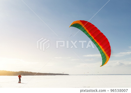 Panoramic view of many people friends enjoy riding kite surf board in warm suit on bright sunny winter day at frozen lake field snowy surface. Wintersport adrenaline fun adventure hobby acitivity Panoramic view of many people friends enjoy riding kite surf board in warm suit on bright sunny winter day at frozen lake field snowy surface. Wintersport adrenaline fun adventure hobby acitivity 96538007
