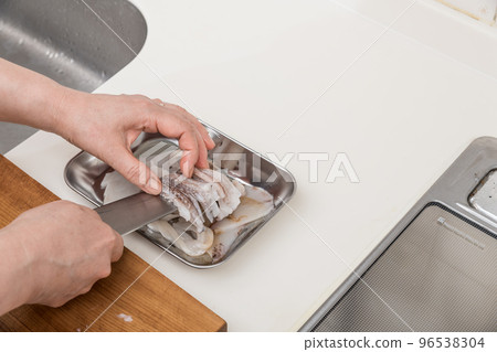 [A middle-aged housewife prepares a squid; she cuts it into a vat] 96538304