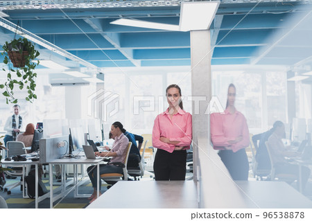 Portrait of young smiling business woman in creative open space coworking startup office. Successful businesswoman standing in office with copyspace. Coworkers working in background. Portrait of young smiling business woman in creative open space coworking startup office. Successful businesswoman standing in office with copyspace. Coworkers working in background. 96538878